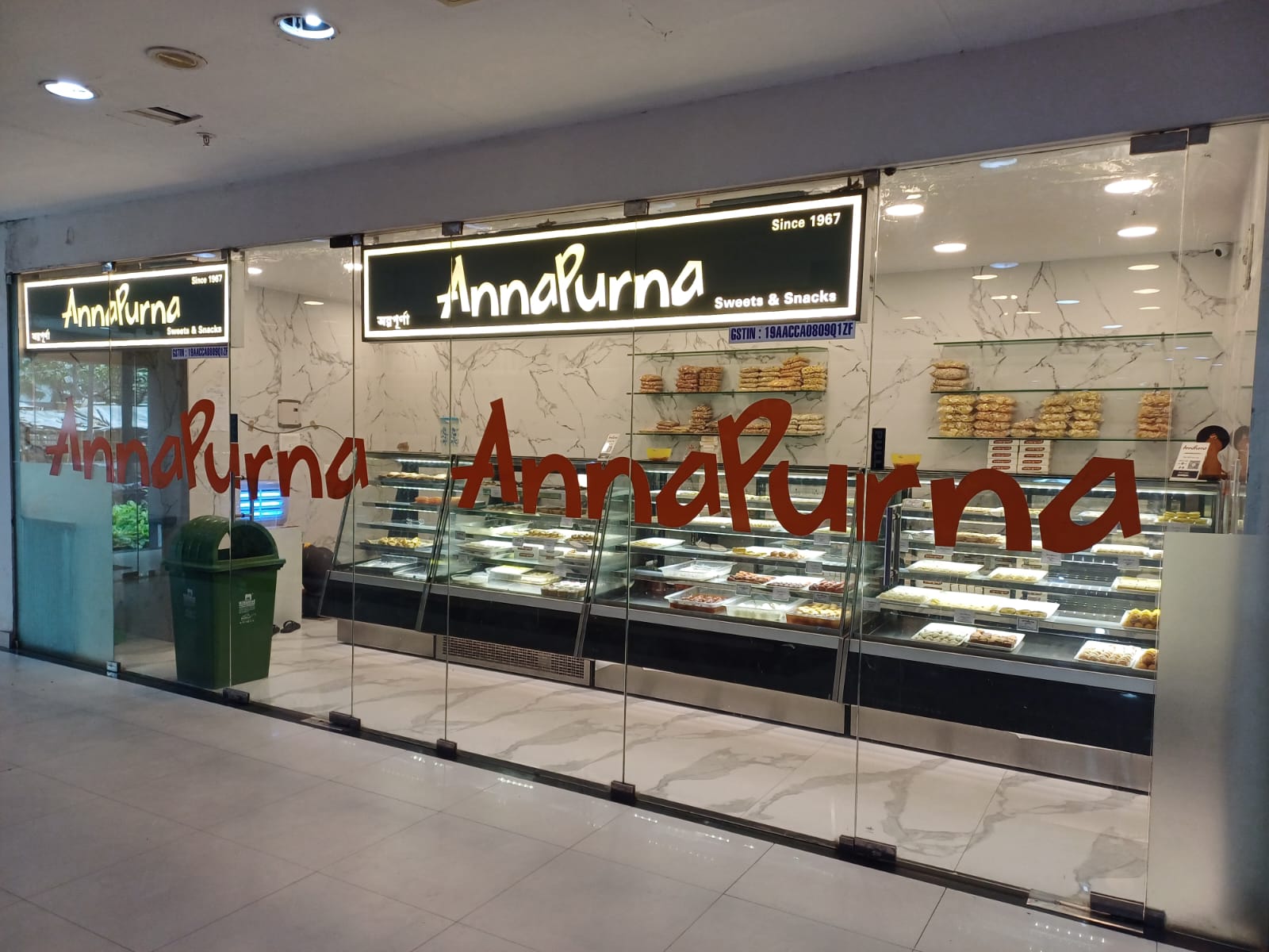 A glass-fronted retail space for "AnnaPurna Sweets & Snacks," showcasing display cases filled with various sweets and snacks.